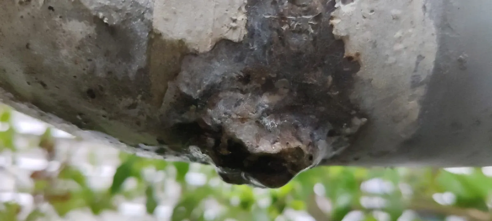Corroded pipe surface with a slow drip forming at the bottom