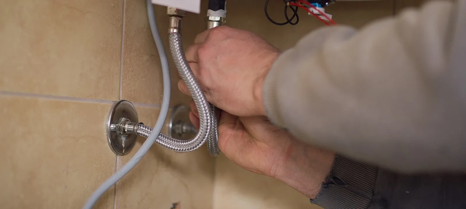 Hands connecting a braided supply line to a wall shutoff valve